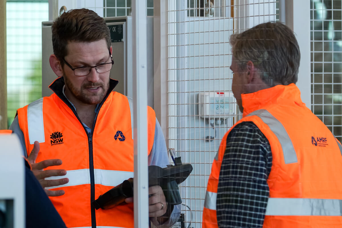Two men wearing high-vis vests talking next to a machine.
